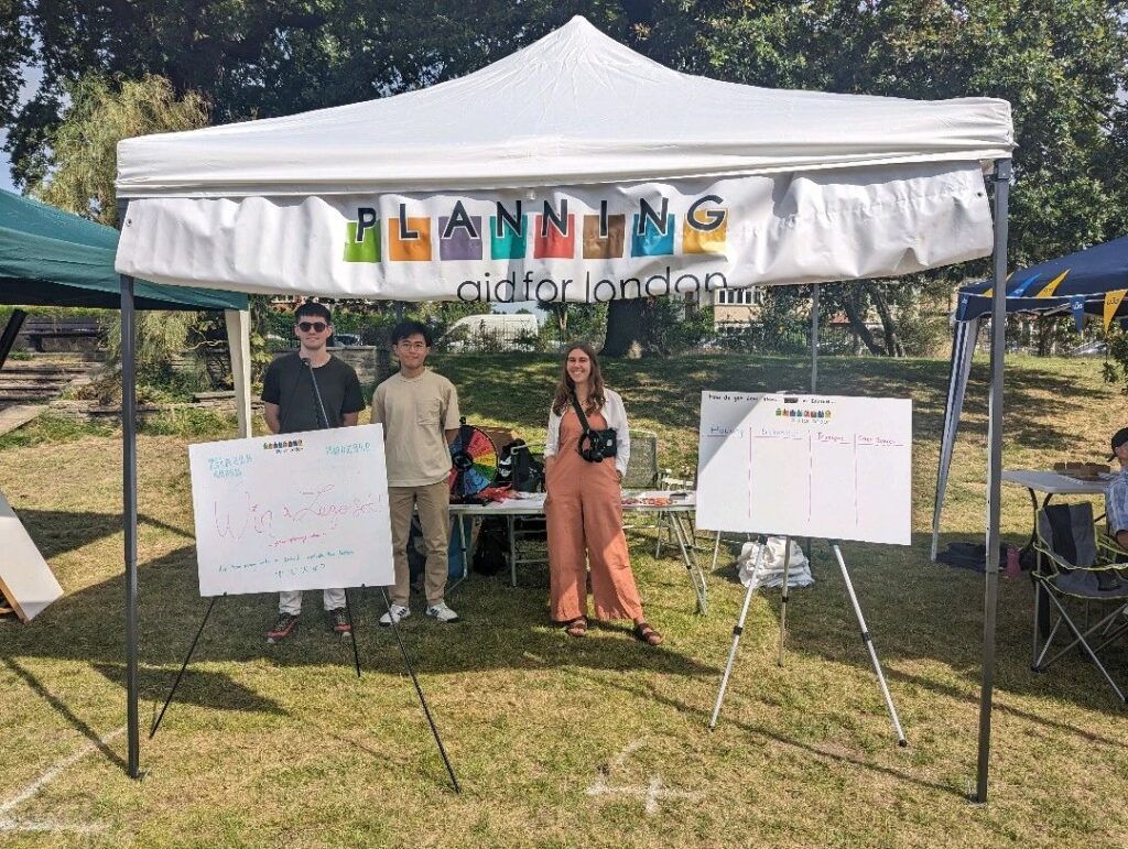 Three volunteers standing after a white gazebo. There are two whiteboards on either side of the people.